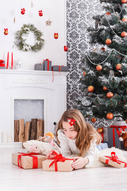 Beautiful girl in santa hat unwrapping christmas presents - Photo, Image