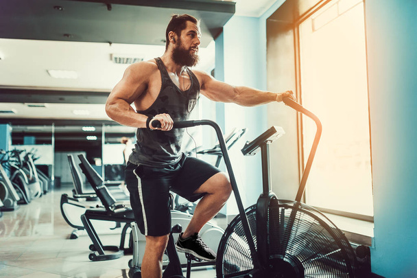 young man using exercise bike at the gym. Fitness male using air bike for cardio workout at crossfit gym. - Foto, Imagem