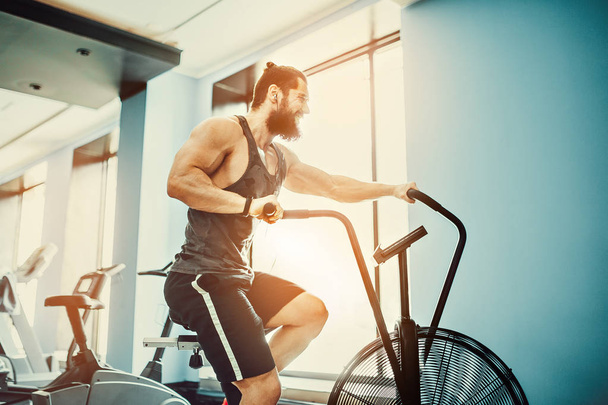 young man using exercise bike at the gym. Fitness male using air bike for cardio workout at crossfit gym. - Foto, Bild