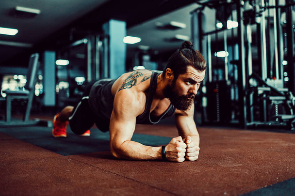 Muscled young man wearing sport wear and doing plank position while exercising on the floor in loft interior - Foto, Imagem