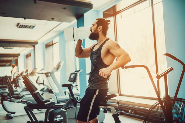 guy relaxing after workout and hold or drink water from big bottle in gym - Foto, immagini
