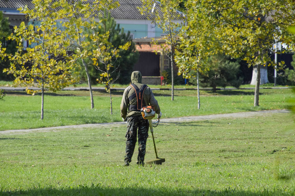 Krasnodar, Russia - October 12, 2016: A worker mowing grass with a gasoline brush. Trimmer. Mowing green grass using a fishing line trimmer. Application trimmers. - Foto, Bild
