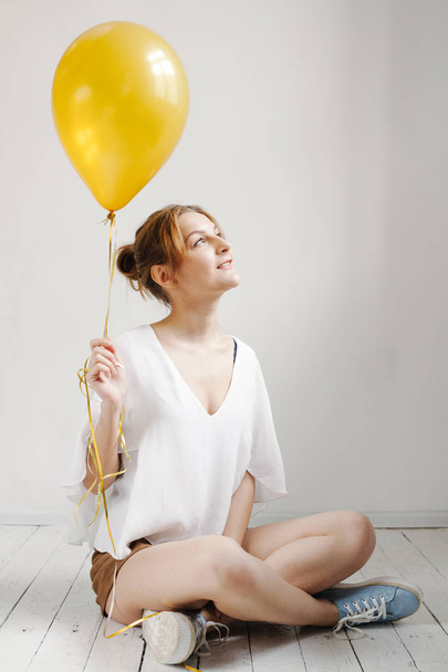 Portrait of cute girl in a studio smiling and playing with yellow balloons, background with copyspace - Photo, Image