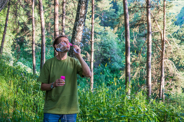 Young man blowing soap bubbles. Man in summer forest in the moun - Photo, Image