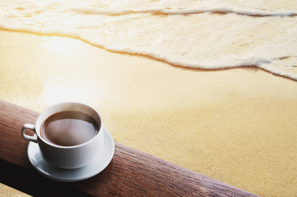 Kop warme koffie drinkt op houten tafel, op het strand in sunrise - Foto, afbeelding