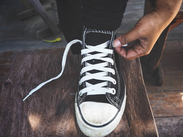 обрезанный снимок человека, завязывающего шнурки кроссовок на деревянной поверхности
 - Фото, изображение