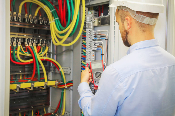 electrical engineer with multimeter on background of distribution cabinet of electrical power cables - Foto, afbeelding