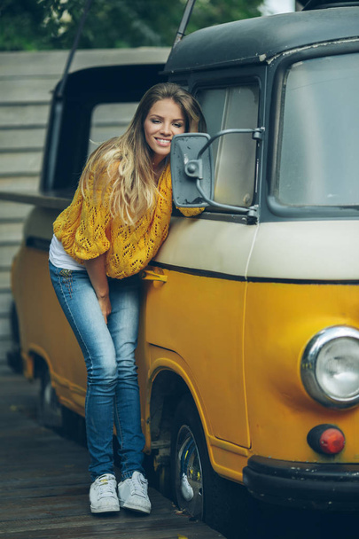 Happy smiling girl is wearing yellow sweater near old retro bus, autumn concept - Foto, immagini