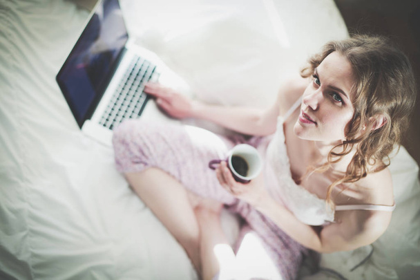 Young beautiful woman sitting in bed with laptop. - Foto, afbeelding