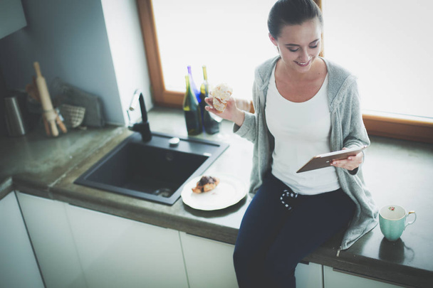 Beautiful young woman using a digital tablet in the kitchen. - Foto, imagen