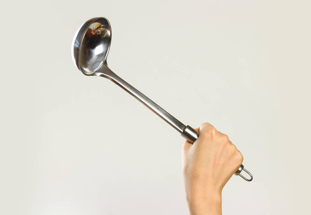 Female hands holding a metal ladle. Isolated on gray background. - Photo, image