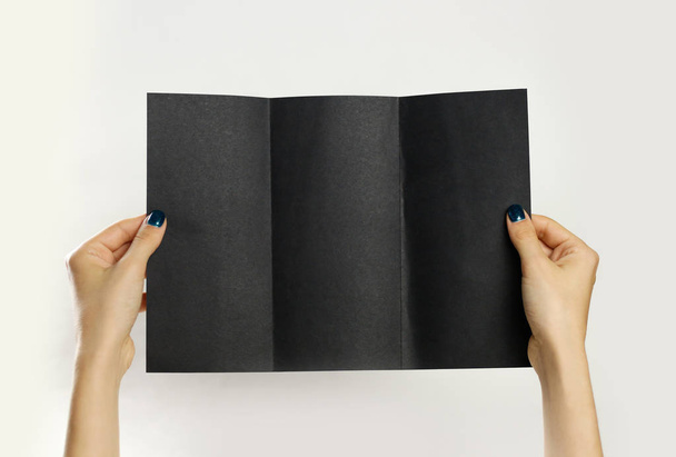 Female hands holding a black booklet triple sheet of paper. Isol - Foto, Imagen