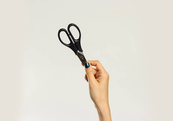 Female hands holding black scissors. Isolated on gray background - Photo, image
