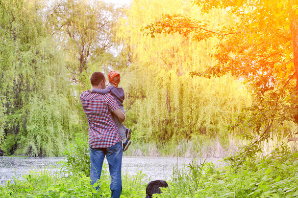 Dad with a little son are standing on the shore of a forest lake, rear view - Photo, Image