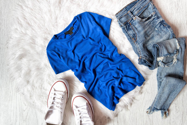 Blauw T-shirt, jeans en witte sneakers geript. Modieuze concept op wit bont - Foto, afbeelding