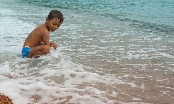 Gelukkige jongen spelen in de zee op het strand. - Foto, afbeelding