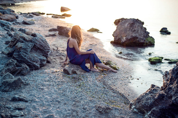 woman sitting on rocky beach - Фото, изображение