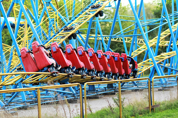Montaña rusa roja que monta en el ferrocarril azul y amarillo contra el cielo azul en el parque de atracciones
 - Foto, imagen