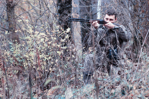 Een man in camouflage en met een jachtgeweer in een forest op een sp - Foto, afbeelding