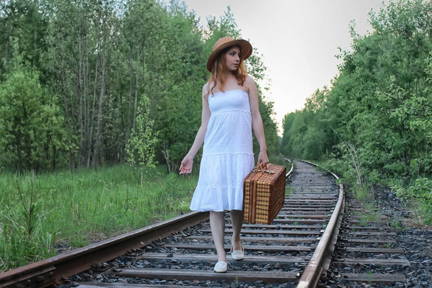 Tyttö valkoinen sundress ja paju matkalaukku kävely kiskoilla
 - Valokuva, kuva