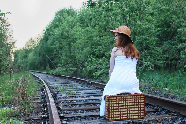 meisje in een witte sundress en rieten koffer lopen op rails - Foto, afbeelding