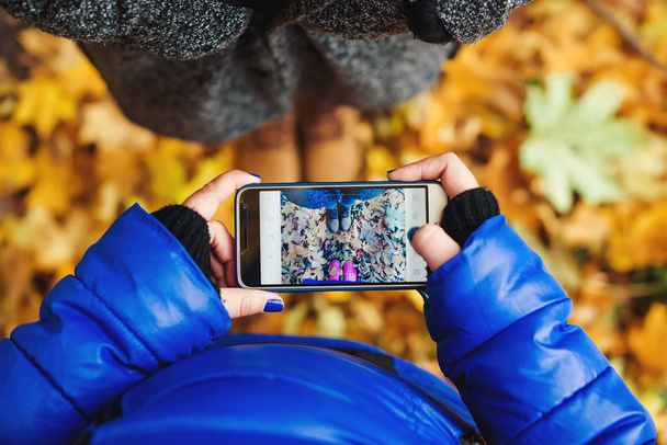Two girls make a photo of shoes by phone in autumn park. Lifestyle and technology concept. - Photo, Image