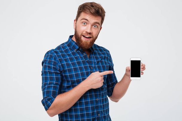 Surprised bearded man in checkered shirt showing blank smartphone screen - 写真・画像