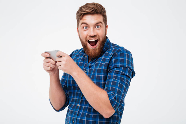 Happy bearded man in checkered shirt playing on his smartphone - Φωτογραφία, εικόνα