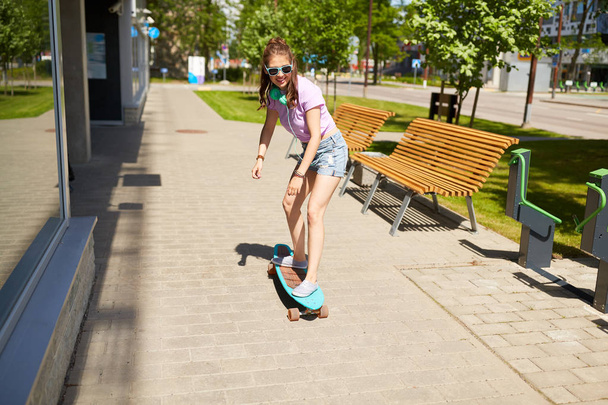 happy teenage girl in shades riding on longboard - Foto, Bild