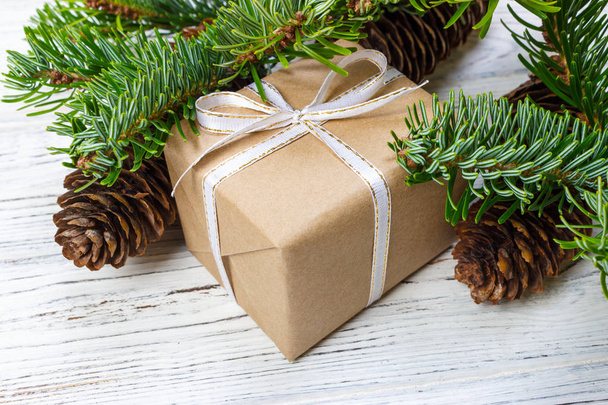 Різдвяна подарункова коробка на фоні білого дерев'яного столу, гілка ялини, конуси сосни, рамка, вид зверху, простір для тексту
 - Фото, зображення