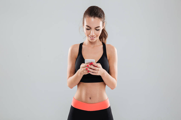 Smiling fitness woman writing message on her smartphone - Photo, image