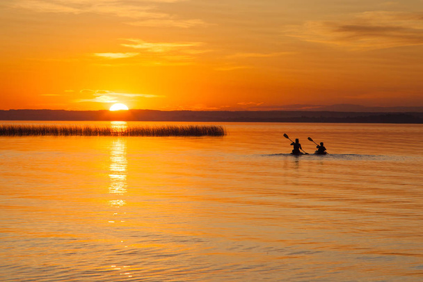 Sylwetka dwóch kajakarzy na jeziorze podczas zachodu słońca - Zdjęcie, obraz
