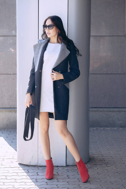 Outdoor portrait of a young beautiful fashionable woman, outdoors. A model dressed in a stylish gray coat, sunglasses. The concept of womens fashion, urban lifestyle - Fotografie, Obrázek