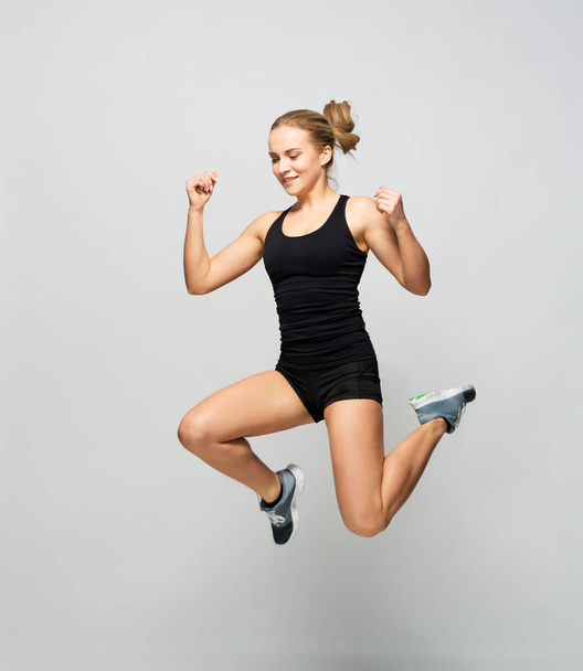young woman in black sportswear jumping - Fotoğraf, Görsel