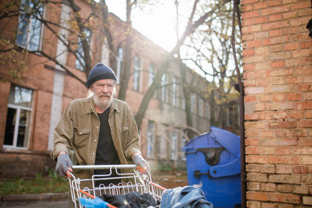 View of homeless old man with cart from supermarket. - Фото, изображение