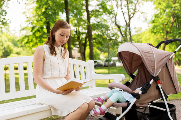 Äiti lapsen kanssa lastenrattaissa lukeminen kirja puistossa
 - Valokuva, kuva