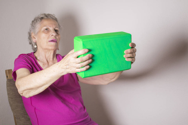 Senior woman doing rehabilitation exercises with a block of yoga - Foto, Imagem