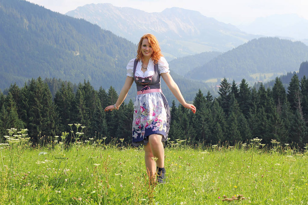 Μια νεαρή κοκκινομάλλα γυναίκα σε ένα dirndl στα βουνά - Φωτογραφία, εικόνα