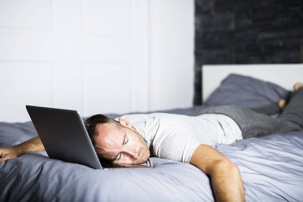 man sleeping over laptop computer in bed - Photo, Image