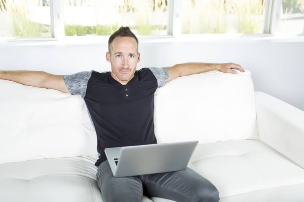Front view of a handsome man using  laptop sitting on couch at home - Foto, immagini