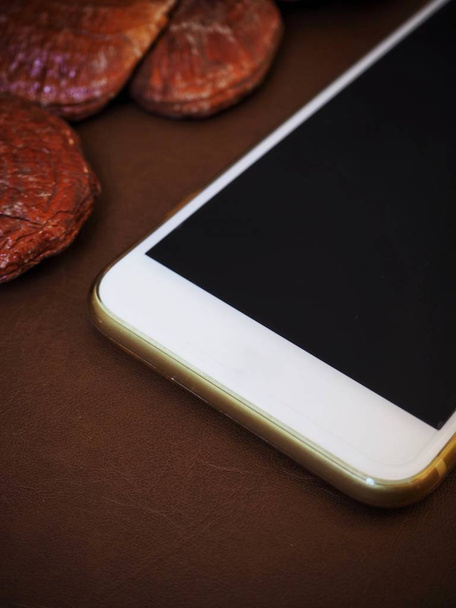 Ganoderma Lucidum Ling Zhi Funghi con smartphone su sfondo pelle marrone
 - Foto, immagini