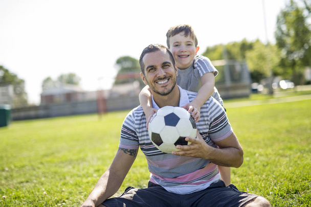 man with child playing football on field - Foto, immagini