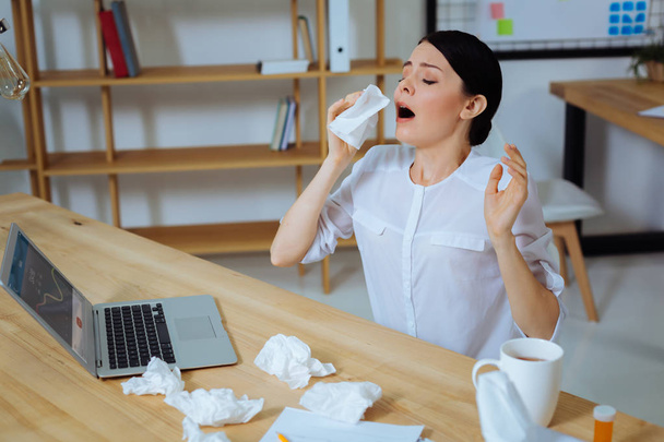 Sick female person sneezing at work - 写真・画像