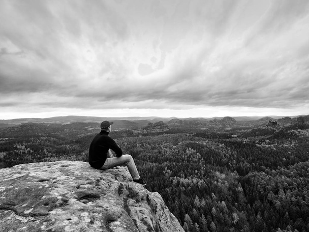 Patrząc na horyzoncie. Człowiek siedzieć na skale powyżej gęstych lasów lub dżungli i cieszyć się widokiem. - Zdjęcie, obraz