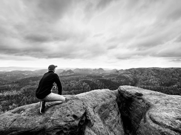 Blick zum Horizont. Mann sitzt auf Felsen über dichten Wäldern oder Dschungel und genießt Aussicht. - Foto, Bild