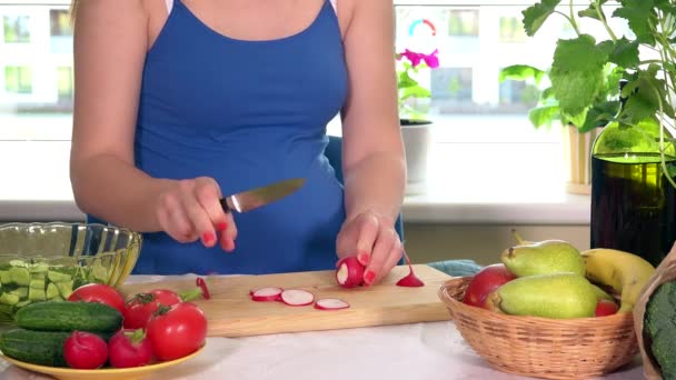 Těhotná žena řezání ředkvičky zelenina na prkénku - Záběry, video