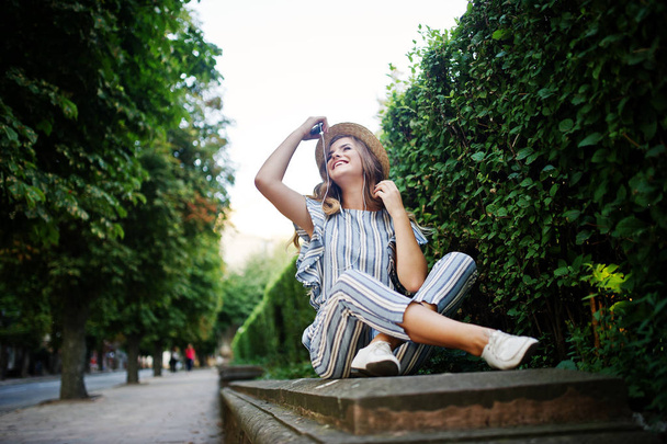 Portrait of a stunning young woman in striped overall sitting in - Фото, изображение