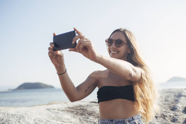 Femme prenant des photos sur la plage avec téléphone portable
  - Photo, image