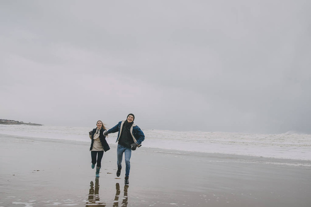 A Young Couple Run Along A Winter Beach - 写真・画像