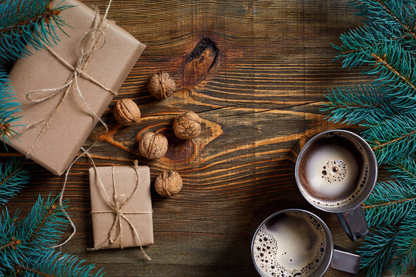 Kerstcadeautjes met twee kopjes cappuccino, noten, kegels en Spar tak op houten achtergrond close-up - Foto, afbeelding